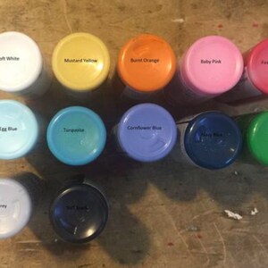 Pu&ograve; includere: Assortimento di barattoli di vernice in vari colori, tra cui bianco morbido, giallo senape, arancione bruciato, rosa tenue, rosso fuoco, blu uovo d'uccello, turchese, blu fiordaliso, blu navy, verde vero e grigio chiaro.