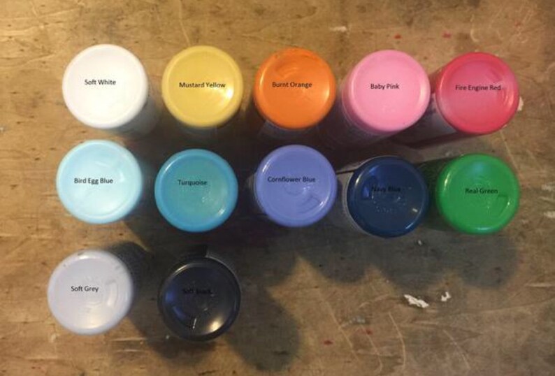 Pu&ograve; includere: Assortimento di barattoli di vernice in vari colori, tra cui bianco morbido, giallo senape, arancione bruciato, rosa tenue, rosso fuoco, blu uovo d'uccello, turchese, blu fiordaliso, blu navy, verde vero e grigio chiaro.