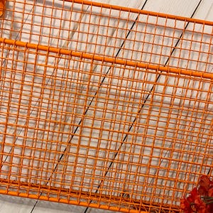 K&ouml;nnte beinhalten: Orangefarbenes Wandregal aus Metalldraht mit einem einzigen Trennelement. Das Regal besteht aus einem Gittermuster und hat eine rechteckige Form.