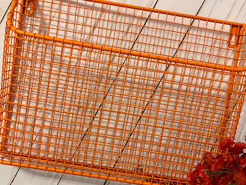 K&ouml;nnte beinhalten: Orangefarbenes Wandregal aus Metalldraht mit einem einzigen Trennelement. Das Regal besteht aus einem Gittermuster und hat eine rechteckige Form.