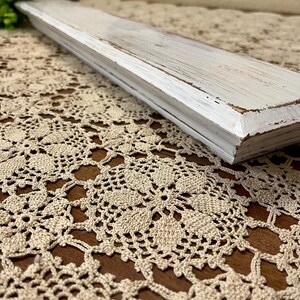 May include: A white wooden shelf with a distressed finish. The shelf is made of reclaimed wood and has a rustic look.