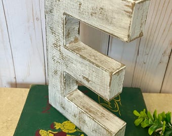 May include: White wooden letter E with a distressed finish. The letter is standing on a green book with the title "FAWN IN THE FOREST".
