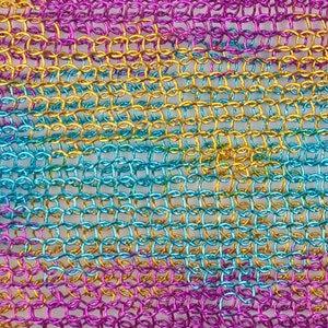 May include: A close-up of a metallic chainmail fabric with a gradient of pink, blue and gold colours.