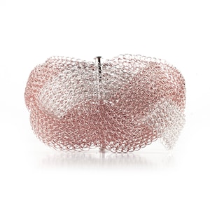 Pode incluir: Uma pulseira tecida com tons prateados e ouro rosa. A pulseira &eacute; feita de pequenas liga&ccedil;&otilde;es met&aacute;licas interconectadas, criando uma apar&ecirc;ncia de malha. Possui um fecho e foi projetada para ser usada no pulso.
