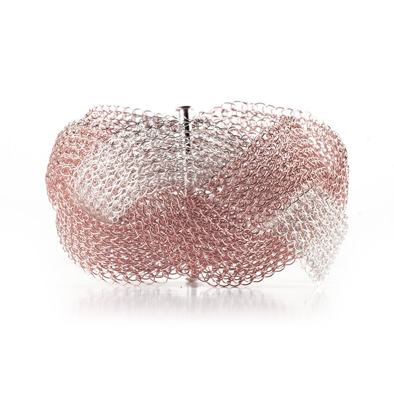 Pode incluir: Uma pulseira tecida com tons prateados e ouro rosa. A pulseira &eacute; feita de pequenas liga&ccedil;&otilde;es met&aacute;licas interconectadas, criando uma apar&ecirc;ncia de malha. Possui um fecho e foi projetada para ser usada no pulso.