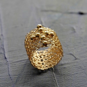 May include: A gold ring crafted from fine wire mesh, adorned with small gold beads.