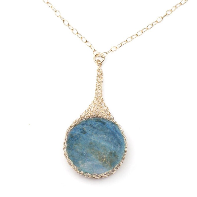 May include: A gold chain necklace with a teardrop-shaped pendant featuring a round blue stone set in a gold wire mesh.