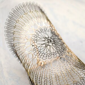 Pode incluir: Um bracelete de fio dourado e preto com um design delicado e intrincado. O bracelete &eacute; feito de fio fino e tem um visual delicado e rendado.