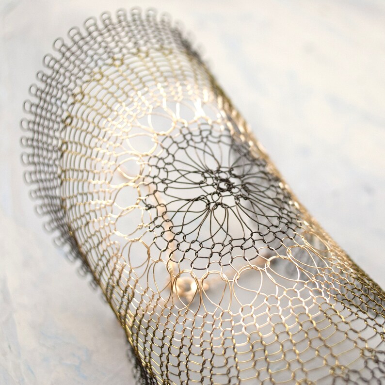 Pode incluir: Um bracelete de fio dourado e preto com um design delicado e intrincado. O bracelete &eacute; feito de fio fino e tem um visual delicado e rendado.