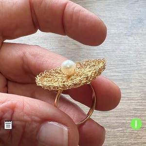 Può includere: Un anello d'oro con un design delicato e intrecciato e una perla bianca al centro.