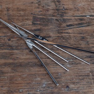May include: A set of five silver crochet hooks with sizes 0.5 mm, 0.75 mm, 1.0 mm, 1.25 mm, and 1.5 mm marked on the hooks.