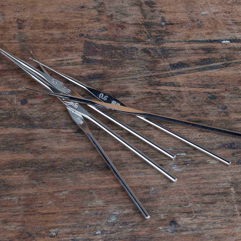 May include: A set of five silver crochet hooks with sizes 0.5 mm, 0.75 mm, 1.0 mm, 1.25 mm, and 1.5 mm marked on the hooks.