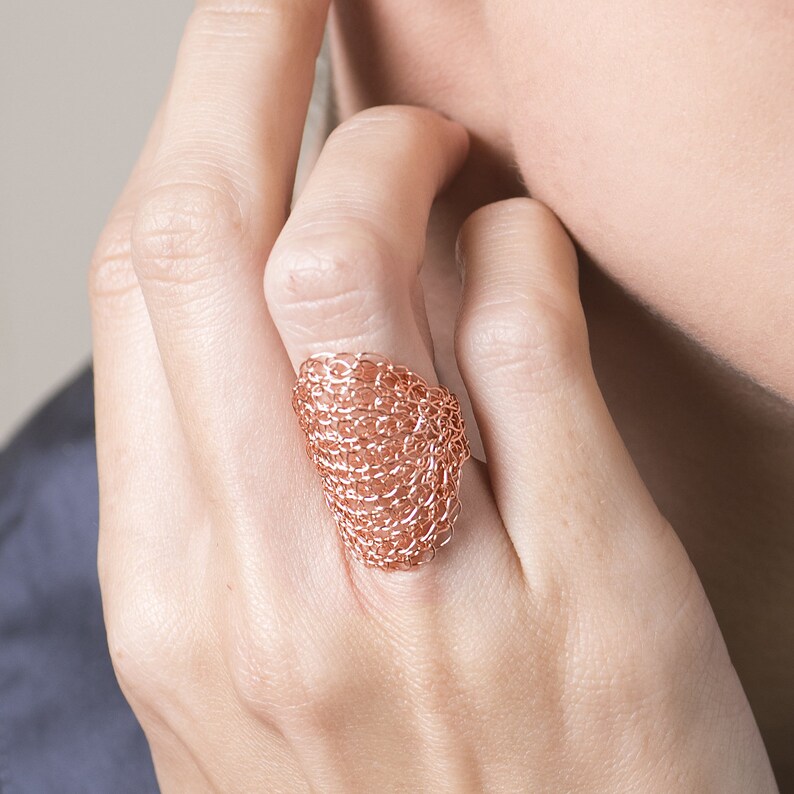 May include: A rose gold wire ring with a delicate, woven design. The ring is worn on a finger.