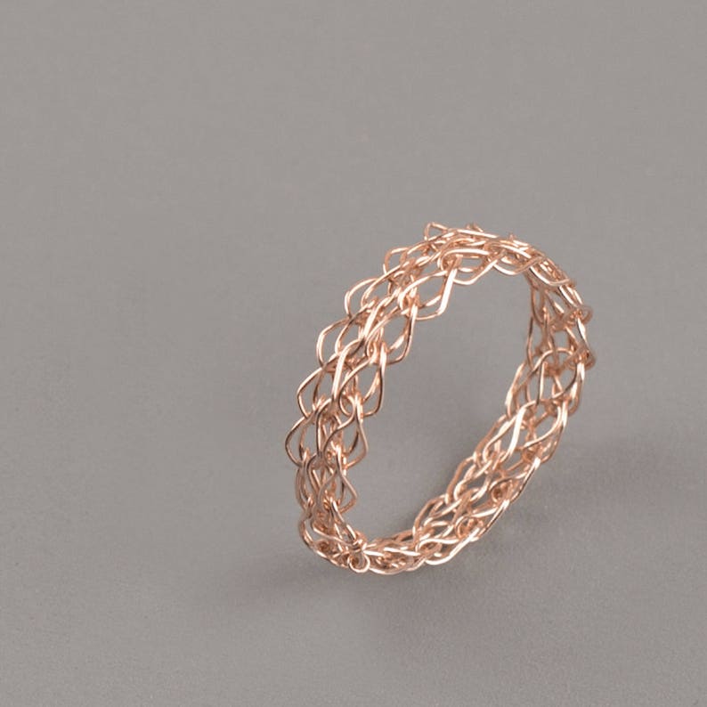 May include: A rose gold ring with a delicate, intricate woven design.