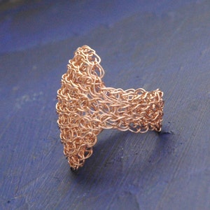 May include: A copper wire ring with a unique, intricate design. The ring is made of woven wire and has a delicate, openwork appearance.
