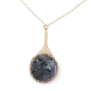 May include: A gold chain necklace with a round, dark gray stone pendant set in a gold wire cage.