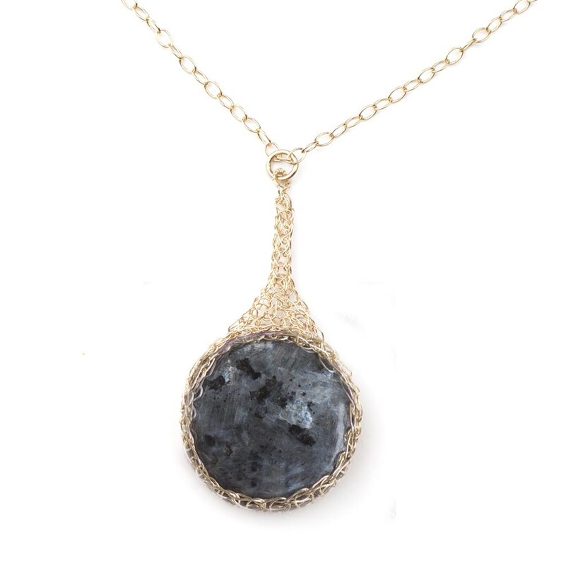 May include: A gold chain necklace with a round, dark gray stone pendant set in a gold wire cage.