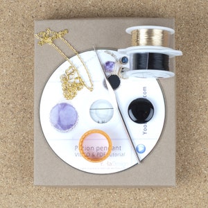 May include: A white CD with a gold chain, purple and black stones, a black and gold wire spool, and a silver crochet hook. The CD has the text "Potion pendant VIDEO & PDF tutorial" and "Y la Design".