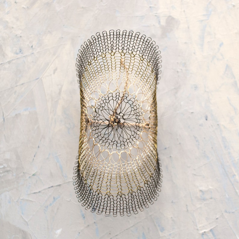 Pode incluir: Um bracelete de malha de arame dourado e preto com um design circular. O bracelete &eacute; feito de arame fino e tem um padr&atilde;o delicado e intrincado.