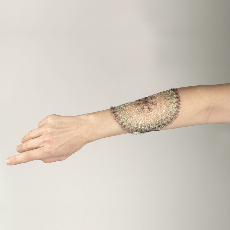Pode incluir: Um bra&ccedil;o com uma pulseira delicada de renda verde e preta no pulso.