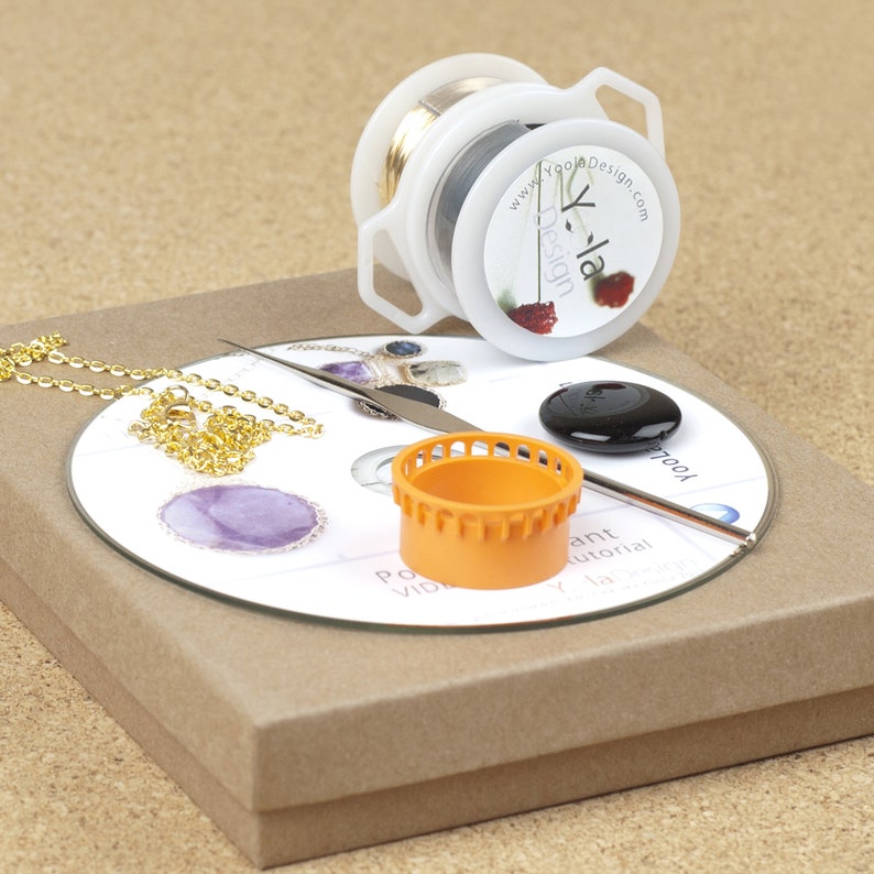 May include: A craft kit for making jewelry, featuring a spool of wire, a chain, a small orange tool, a black stone, and a CD with a tutorial. The CD has the text "Yola Design" and "www.YolaDesign.com".