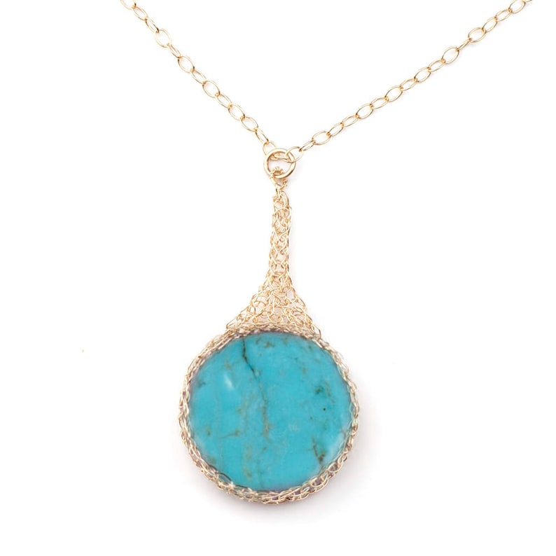 May include: A gold chain necklace with a turquoise stone pendant. The pendant is surrounded by a delicate gold wire design.
