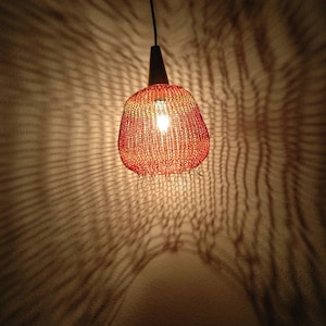May include: A red and orange crocheted lampshade hangs from a ceiling, casting a patterned shadow on the wall.