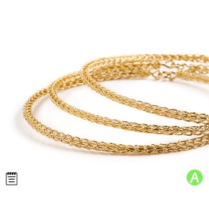 May include: Three gold chain bracelets, each with a different width, are stacked on top of each other. The bracelets are made of a delicate, woven chain.
