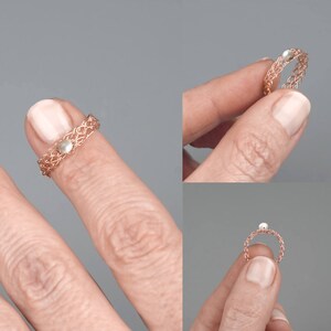 May include: A delicate rose gold ring with a small pearl accent. The ring is shown on a finger.