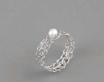May include: A silver ring with a delicate, woven design and a single white pearl in the center.