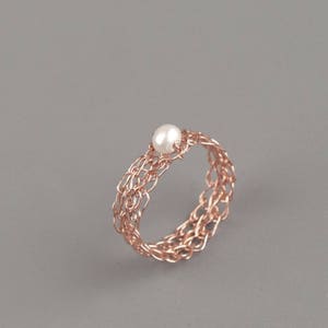 May include: A rose gold wire ring with a delicate woven design and a single white pearl in the center.