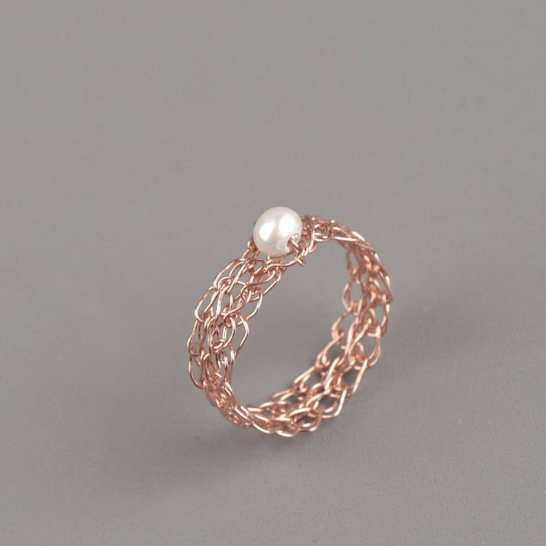 May include: A rose gold wire ring with a delicate woven design and a single white pearl in the center.