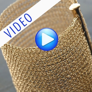 May include: A gold metal bracelet made of chainmail. The bracelet is open and has a metal clasp.