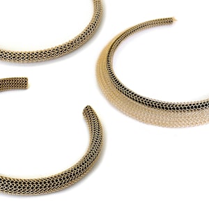 May include: Three gold chain necklaces with black and white mesh designs. The necklaces are arranged in a semi-circle on a white background.
