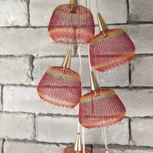 May include: A set of six red, orange, and green woven pendant lights with gold accents. The lights are hanging from a white brick wall.