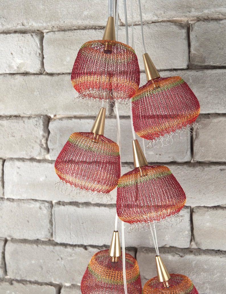 May include: A set of six red, orange, and green woven pendant lights with gold accents. The lights are hanging from a white brick wall.