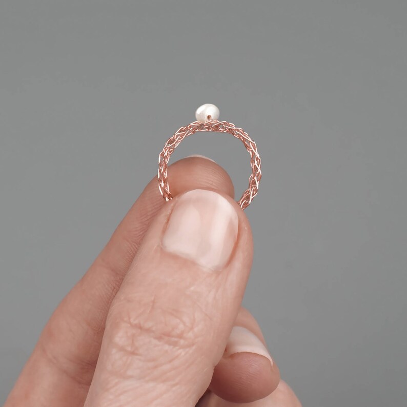 May include: A rose gold ring with a braided design and a single white pearl in the center.
