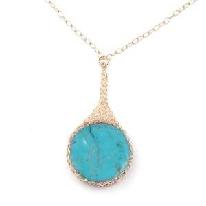 May include: A gold chain necklace with a turquoise stone pendant. The pendant is surrounded by a delicate gold wire design.