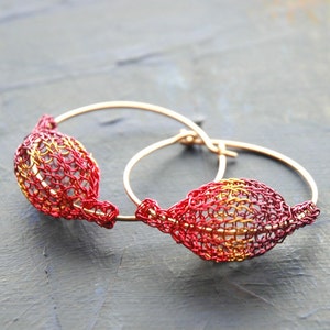 May include: A pair of gold hoop earrings with red and gold wire mesh accents. The earrings are delicate and feminine.