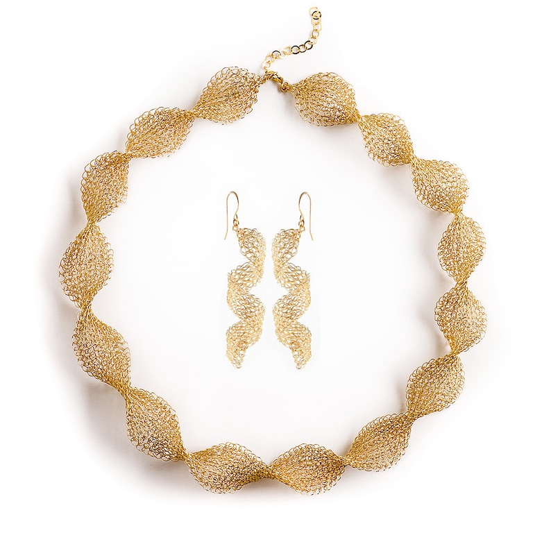 May include: A gold necklace and matching earrings made of delicate, interwoven metal. The necklace is a long, twisted chain with a clasp closure. The earrings are long and dangle, with a similar twisted design.