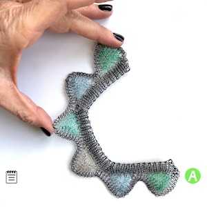 May include: A black wire necklace with green and blue accents. The necklace is made of wire and has a geometric design.