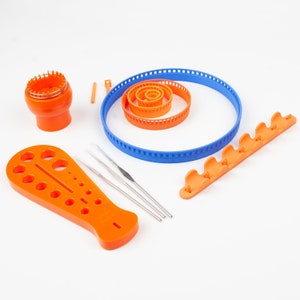 May include: A set of orange and blue knitting tools, including a circular loom, a set of needles, a gauge tool, and a set of stitch markers.