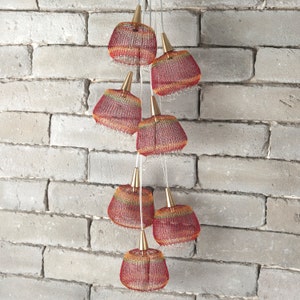 May include: A multi-tiered pendant light fixture with six red, orange, and yellow woven lampshades.