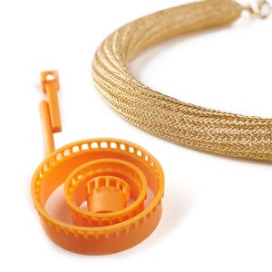 May include: A close-up of a gold chain necklace and an orange plastic knitting loom. The chain is made of small, interwoven metal links. The loom is a circular tool with multiple concentric rings.