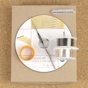 Puede incluir: Una caja marr&oacute;n con un CD blanco en su interior. El CD tiene una cadena dorada, un gancho plateado y dos carretes de alambre plateado en la parte superior. La caja tiene el texto "ToolaCuff VIDEO & PDF tutorial Y. la Design all rights reserved to Yael Falk aka Yoola 15 com" impreso en ella.