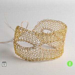 May include: A gold wire mask with a delicate chainmail design. The mask is made of small, interconnected loops of wire, creating a lightweight and intricate pattern.