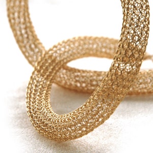 May include: Two gold-colored metal rings, woven in a delicate, intricate pattern, are intertwined. The rings are smooth and shiny, with a subtle sheen.
