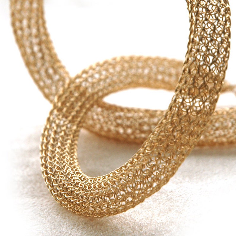May include: Two gold-colored metal rings, woven in a delicate, intricate pattern, are intertwined. The rings are smooth and shiny, with a subtle sheen.
