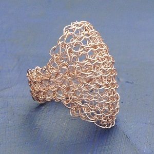 May include: A rose gold wire ring with a delicate, openwork design. The ring is made of fine wire that is woven together to create a unique and intricate pattern.