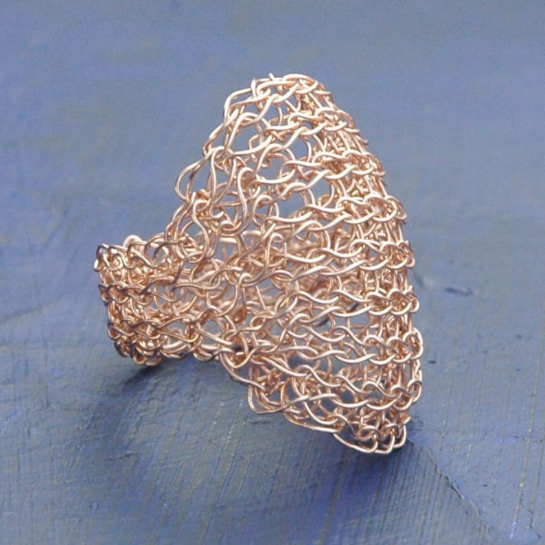 May include: A rose gold wire ring with a delicate, openwork design. The ring is made of fine wire that is woven together to create a unique and intricate pattern.